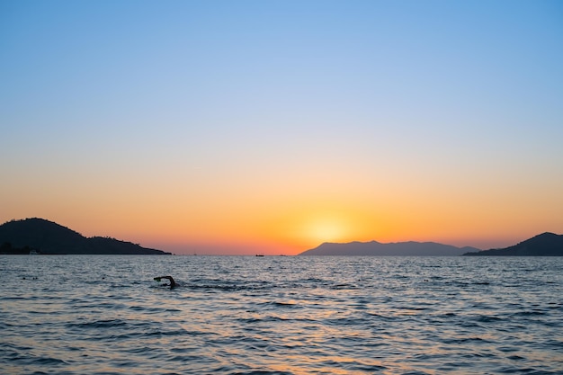 Silhouette eines Schwimmers, der im Meer trainiert, vor dem Hintergrund eines Sonnenuntergangs über der Bucht, die Idee für einen Bildschirmschoner oder eine Werbung für einen Urlaub am Meer