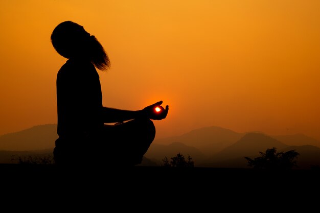 Silhouette - Yoga-Junge auf dem Dach während des Sonnenuntergangs, er praktiziert Yoga.