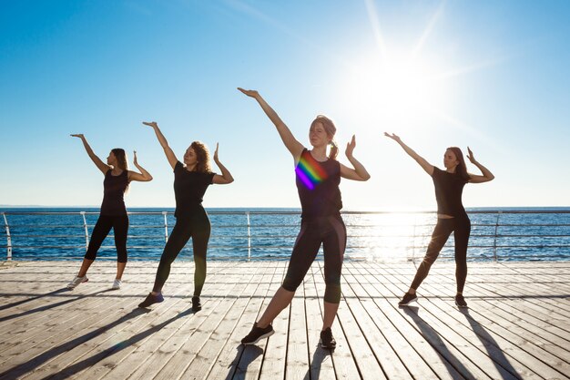 Silhouetten von sportlichen Frauen, die nahe Meer bei Sonnenaufgang tanzen