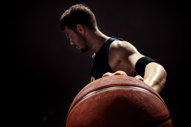 Silhouettieren Sie Ansicht eines Basketball-Spielers, der Korbball auf schwarzer Wand hält