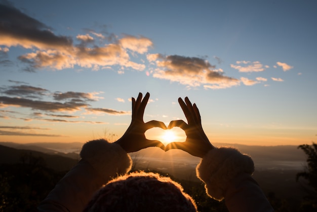 Silhouettieren Sie die Hände, die eine Herzform mit Sonnenaufgang bilden