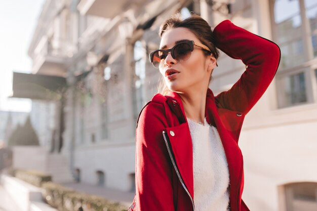 Sinnliche Frau in der großen Sonnenbrille, die mit ihren Haaren am sonnigen Tag spielt