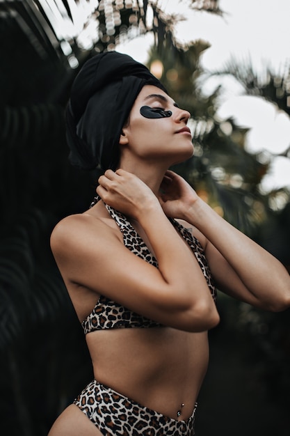 Sinnliche junge Frau mit Augenklappen, die auf Naturhintergrund stehen. Außenaufnahme der inspirierten Frau im schwarzen Turban.