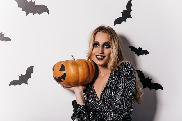 Sinnliche junge Frau mit schwarzem Make-up, das Kürbis hält. spektakuläres Mädchen, das sich auf Halloween-Party vorbereitet.