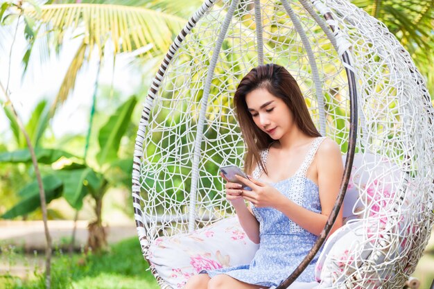 Sitzender Gebrauch Smartphone der jungen Frau im weißen Schwingen