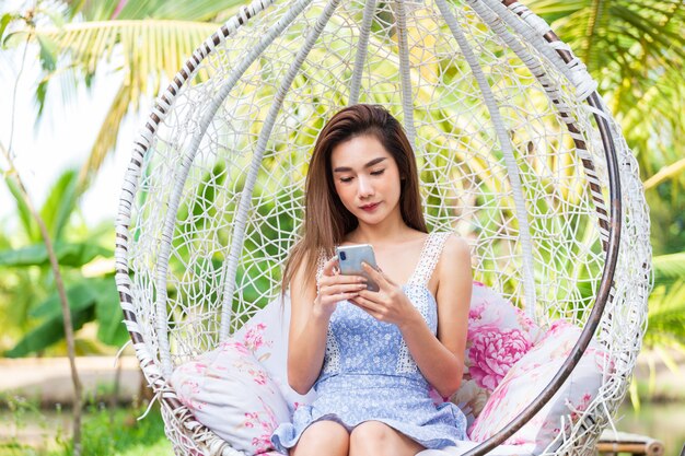 Sitzender Gebrauch Smartphone der jungen Frau im weißen Schwingen