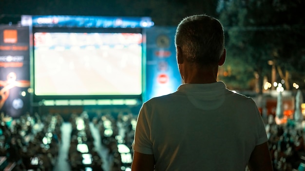 Sitzender Mann, der nachts an einem öffentlichen Ort Fußball guckt