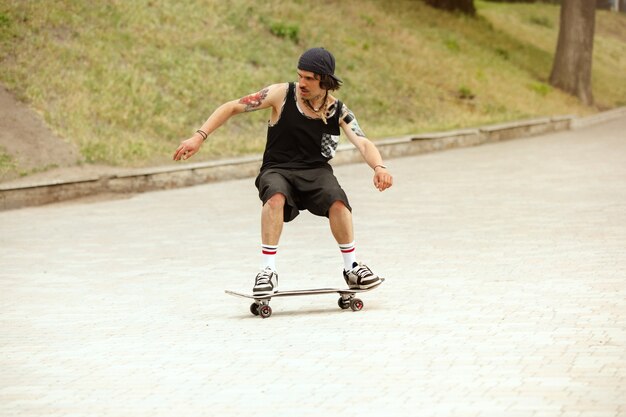 Skateboarder machen an bewölkten Tagen einen Trick auf der Straße der Stadt. Junger Mann in Turnschuhen und Mütze reiten und Longboarding auf dem Asphalt. Konzept von Freizeitbeschäftigung, Sport, Extrem, Hobby und Bewegung.