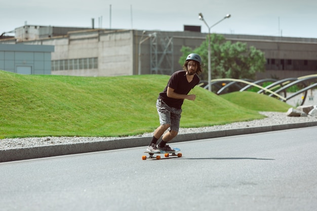 Skateboarder macht an einem sonnigen Tag einen Trick auf der Straße der Stadt. Junger Mann im Ausrüstungsreiten und Longboarden auf dem Asphalt in Aktion. Konzept von Freizeitbeschäftigung, Sport, Extrem, Hobby und Bewegung.