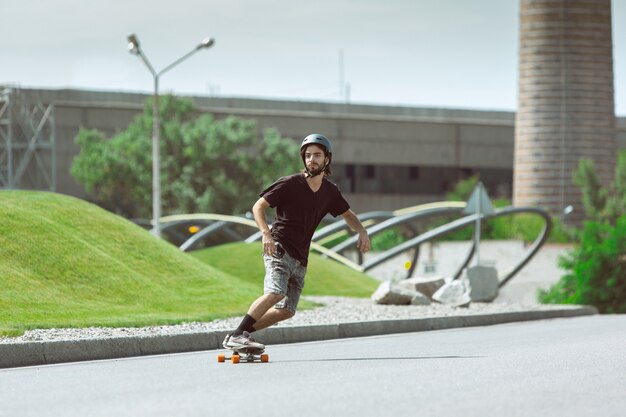 Skateboarder macht an einem sonnigen Tag einen Trick auf der Straße der Stadt. Junger Mann im Ausrüstungsreiten und Longboarden auf dem Asphalt in Aktion. Konzept von Freizeitbeschäftigung, Sport, Extrem, Hobby und Bewegung.