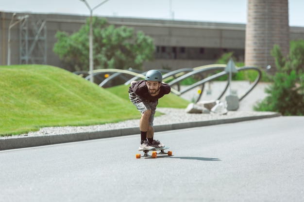 Kostenloses Foto skateboarder macht an einem sonnigen tag einen trick auf der straße der stadt. junger mann im ausrüstungsreiten und longboarden auf dem asphalt in aktion. konzept von freizeitbeschäftigung, sport, extrem, hobby und bewegung.