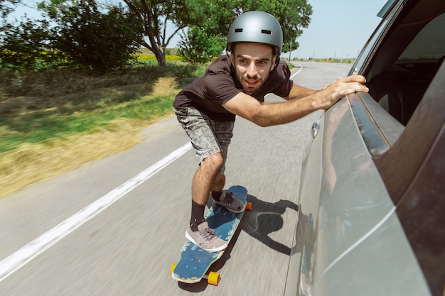 Skateboarder macht an sonnigen Tagen einen Trick auf der Straße der Stadt. Junger Mann in Ausrüstungsreiten und Longboarding in Aktion. Konzept von Freizeitbeschäftigung, Sport, Extrem, Hobby und Bewegung. So schnell wie ein Auto.