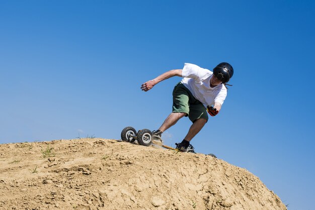 Skateboarder springt mit Mountainboard über den Hügel mit blauem Himmel