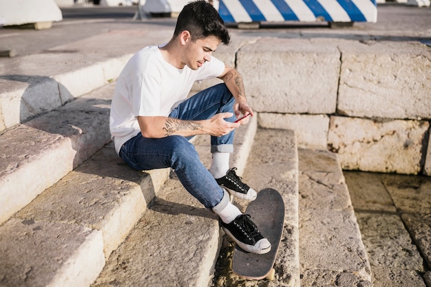 Skateboardfahrer, der auf Treppenhaus mit seinem Handy sitzt