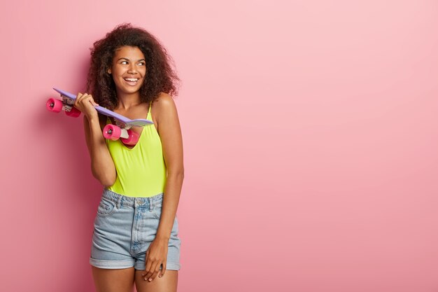 Skater Teenager-Mädchen mit Afro-Frisur, dunkle Haut, trägt Longboard, bereit, Trick auszuführen