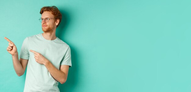 Kostenloses Foto skeptischer kaukasier mit roten haaren und bart, der eine brille und ein t-shirt trägt und nach links schaut und zeigt