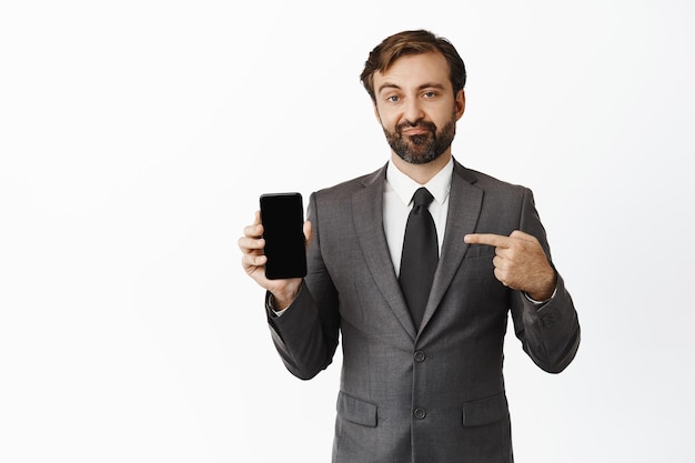 Skeptischer Verkäufer, der mit dem Finger auf den Telefonbildschirm zeigt und das Gesicht verzieht, enttäuschte die negative Meinung über die App, die über weißem Hintergrund steht