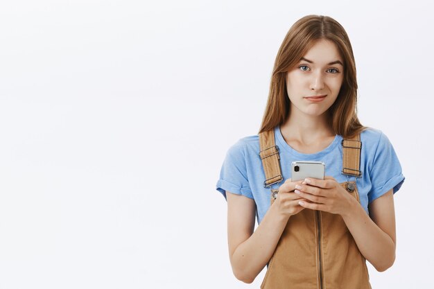 Skeptisches und unzufriedenes Mädchen, das ungerührt grinst und ein Handy in der Hand hält