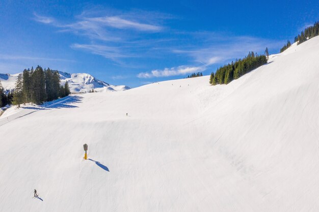 Skigebiet mit Skifahrern, die unter einem blauen Himmel den schneebedeckten Hang hinunterrutschen