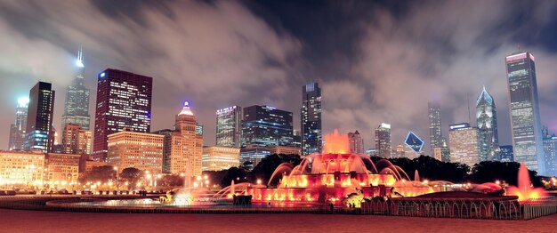 Skyline-Panorama von Chicago mit Wolkenkratzern und Buckingham-Brunnen im Grant Park bei Nacht, beleuchtet von bunten Lichtern.