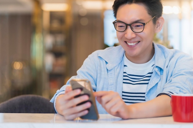 Smart attraktive asiatische Brille männliches Lächeln Glück bei der Verwendung von Smartphone-Kommunikation nach Hause Hintergrund Technologie Ideen Konzept