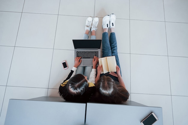 Smartphone, Laptop und Buch. Draufsicht der jungen Leute in der Freizeitkleidung, die im modernen Büro arbeiten