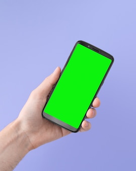 Smartphone mit grünem bildschirm in der rechten hand auf lila hintergrund, abgewinkelte position.