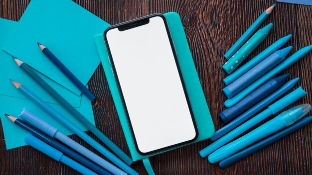 Smartphone mit leerem Bildschirm auf Tagebuch nahe blauen Anstrichfarben und -papier über Holztisch