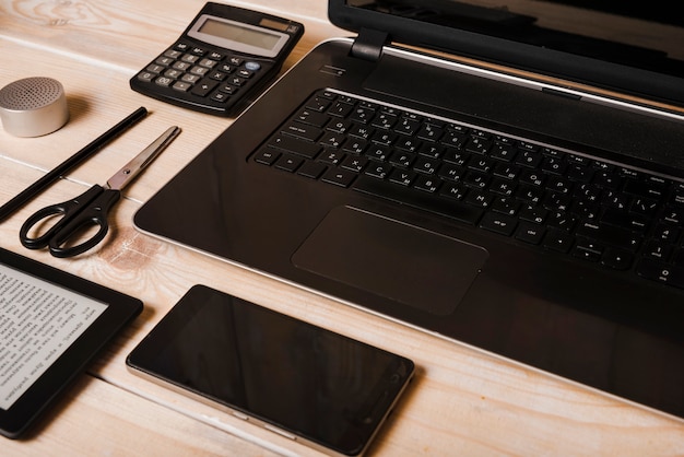 Smartphone; Schere; Taschenrechner; Stift; Laptop- und Ebook-Reader auf Schreibtisch aus Holz