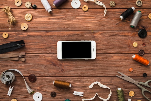 Smartphone umgeben von verschiedenen Nähzubehör auf Holzoberfläche