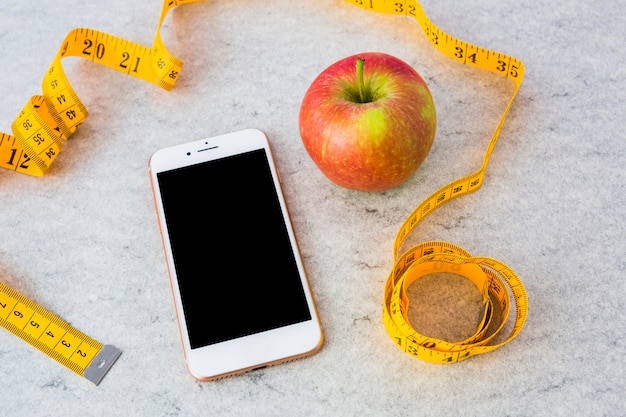 Kostenloses Foto smartphone und roter reifer apfel mit gelbem messendem band auf grauem strukturiertem hintergrund