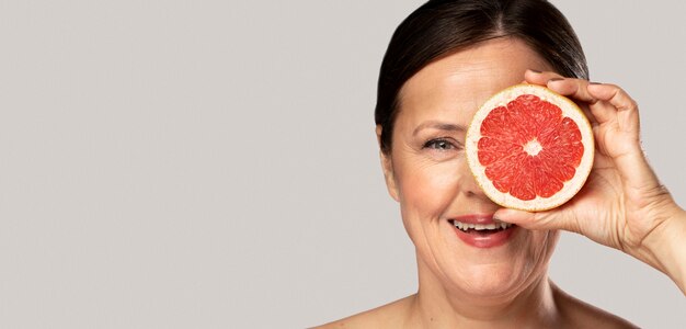 Smiley ältere Frau, die ihr Auge mit der Hälfte der Grapefruit bedeckt