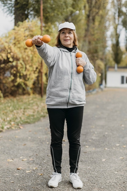 Smiley ältere Frau, die mit Gewichten außerhalb trainiert