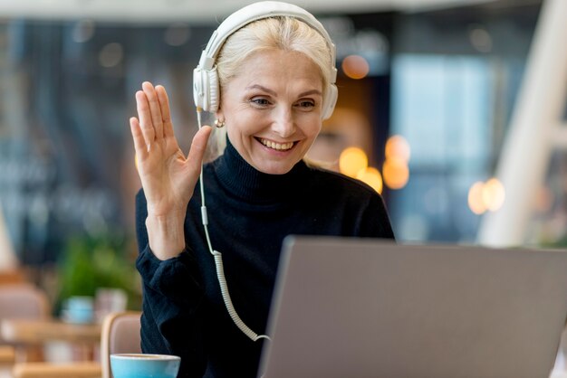 Smiley ältere Geschäftsfrau, die einen Videoanruf auf Laptop mit Kopfhörern hat