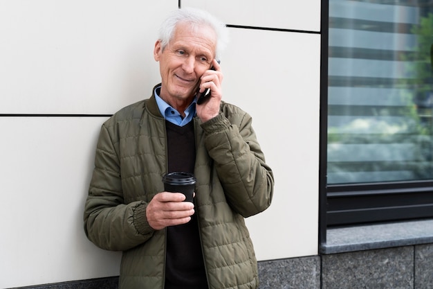 Smiley älterer Mann in der Stadt, der beim Kaffeetrinken auf dem Smartphone spricht