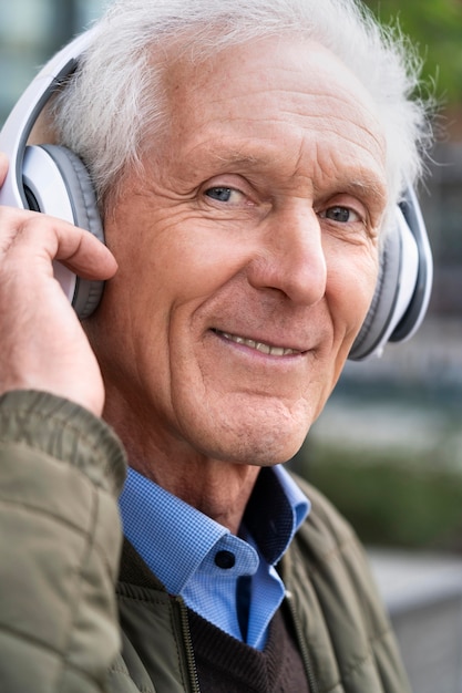 Smiley älterer Mann in der Stadt, der Musik über Kopfhörer hört