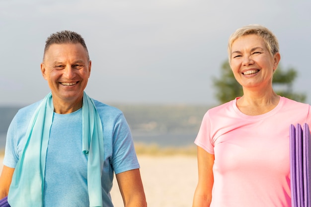 Smiley älteres Paar mit Trainingsausrüstung am Strand