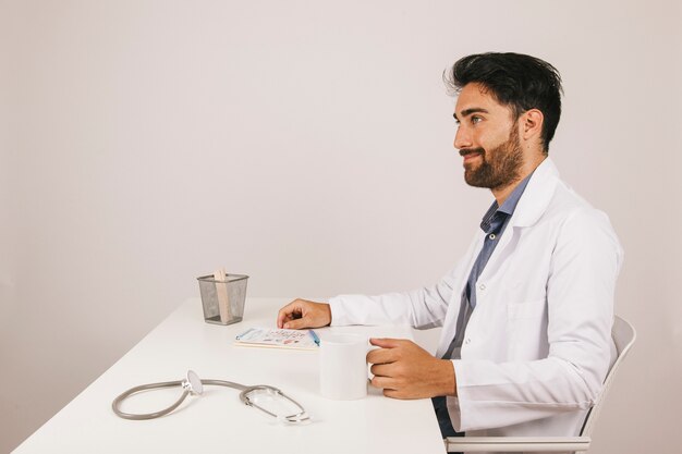Smiley Arzt trinkt Kaffee an seinem Schreibtisch