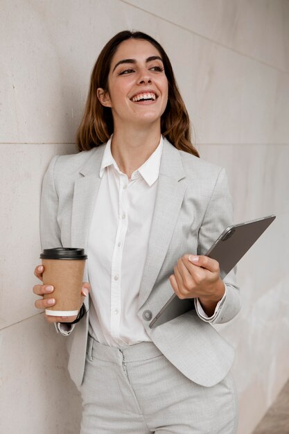 Smiley elegante Geschäftsfrau, die Tablette und Kaffeetasse hält