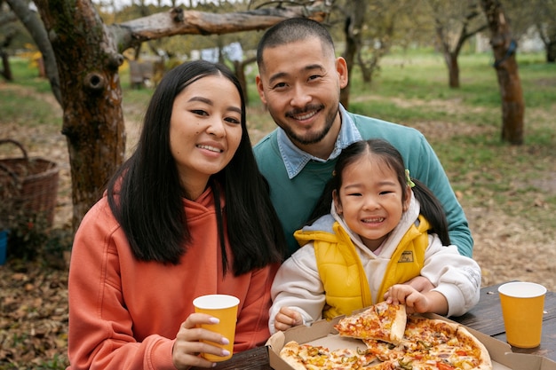 Smiley-Familie mit mittlerem Schuss, die draußen Pizza isst