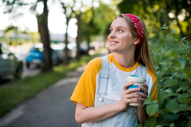 Smiley-Frau, die draußen mit Tasse aufwirft