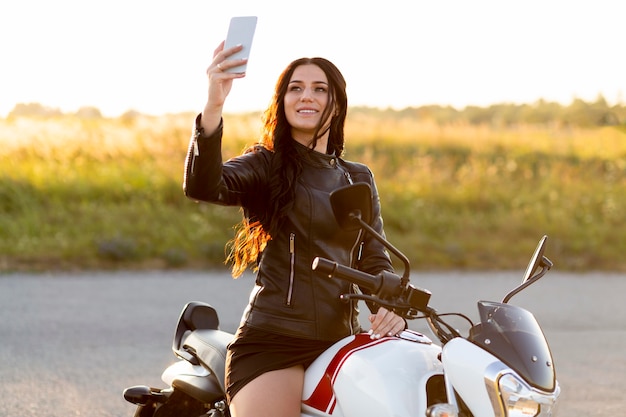 Kostenloses Foto smiley-frau, die ein selfie nimmt, während sie auf ihrem motorrad sitzt