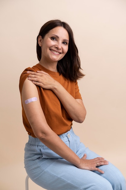 Smiley-Frau, die einen Aufkleber am Arm zeigt, nachdem sie einen Impfstoff bekommen hat