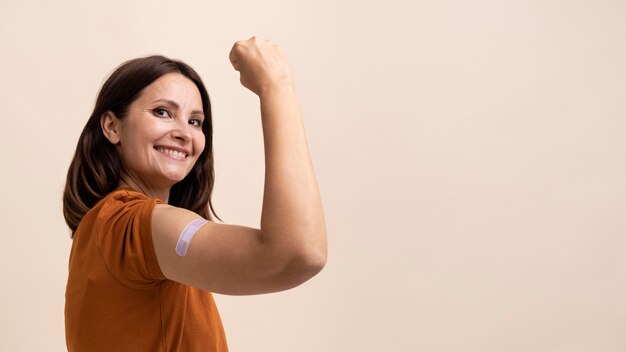 Smiley-Frau, die einen Aufkleber am Arm zeigt, nachdem sie einen Impfstoff bekommen hat