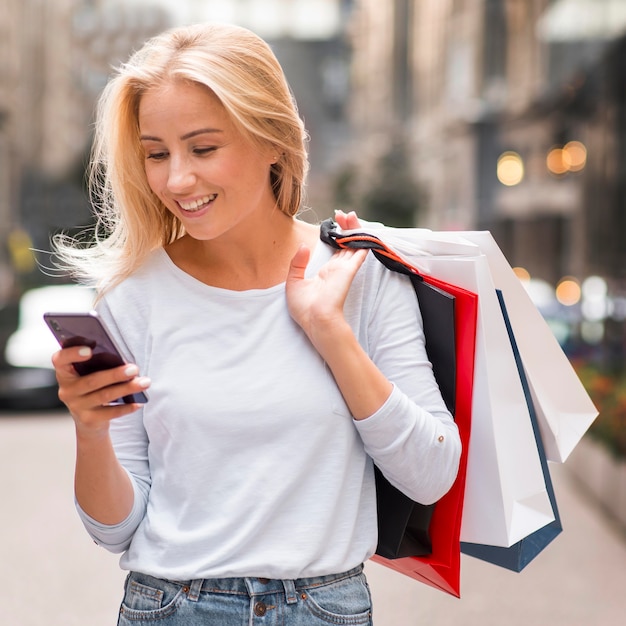 Smiley-Frau, die Einkaufstaschen hält und Smartphone betrachtet