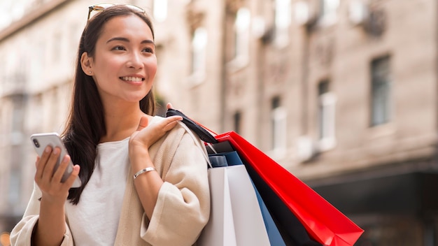 Smiley-Frau, die Einkaufstaschen und Smartphone draußen hält