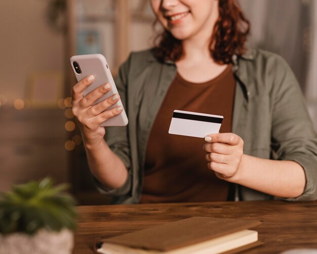 Smiley-Frau, die ihr Smartphone mit Kreditkarte zu Hause benutzt