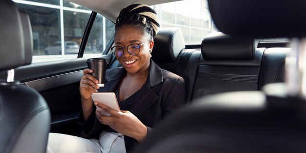 Smiley-Frau, die Kaffee trinkt und Smartphone von ihrem Auto betrachtet