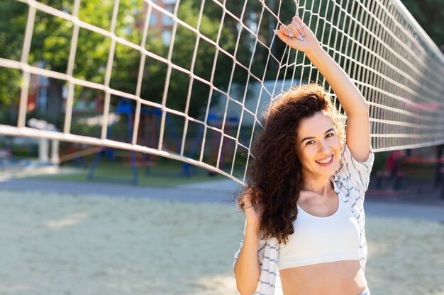 Kostenloses Foto smiley-frau, die neben einem volleyballfeld aufwirft