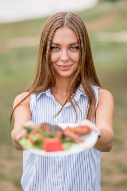 Kostenloses Foto smiley-frau, die platte mit grill draußen hält